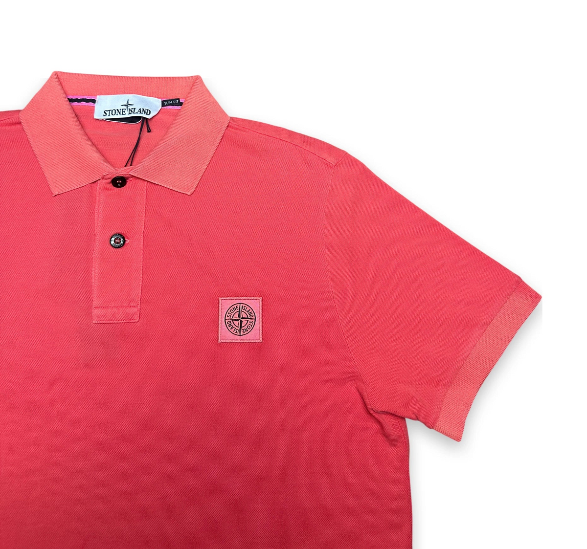 A coral pink short-sleeve polo shirt by Stone Island, featuring a classic collar, two-button placket, and the brand's signature compass logo patch on the left chest, displayed on a clean white background.