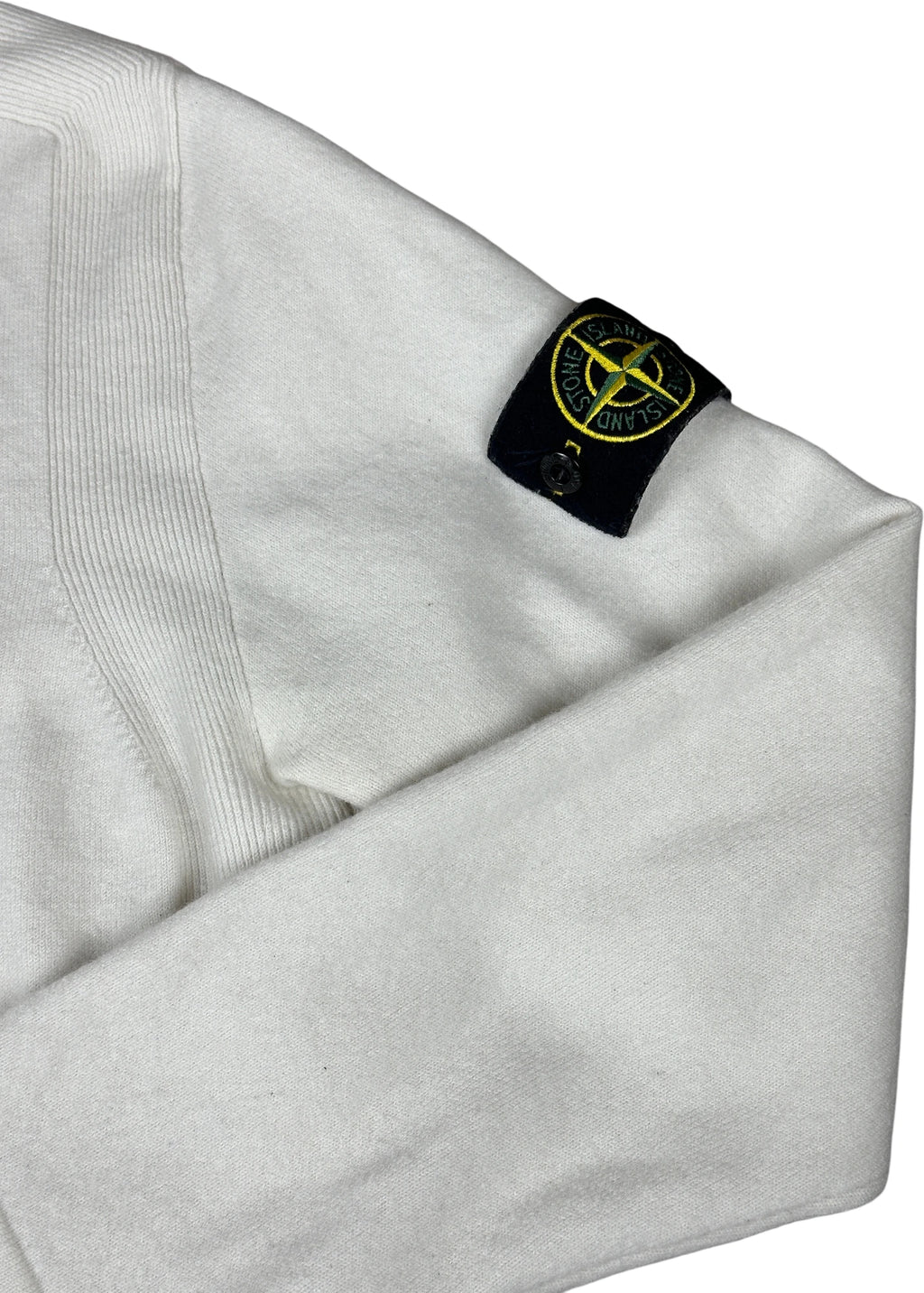 Close-up of a white Stone Island garment sleeve with the brand's signature black compass patch featuring yellow detailing.