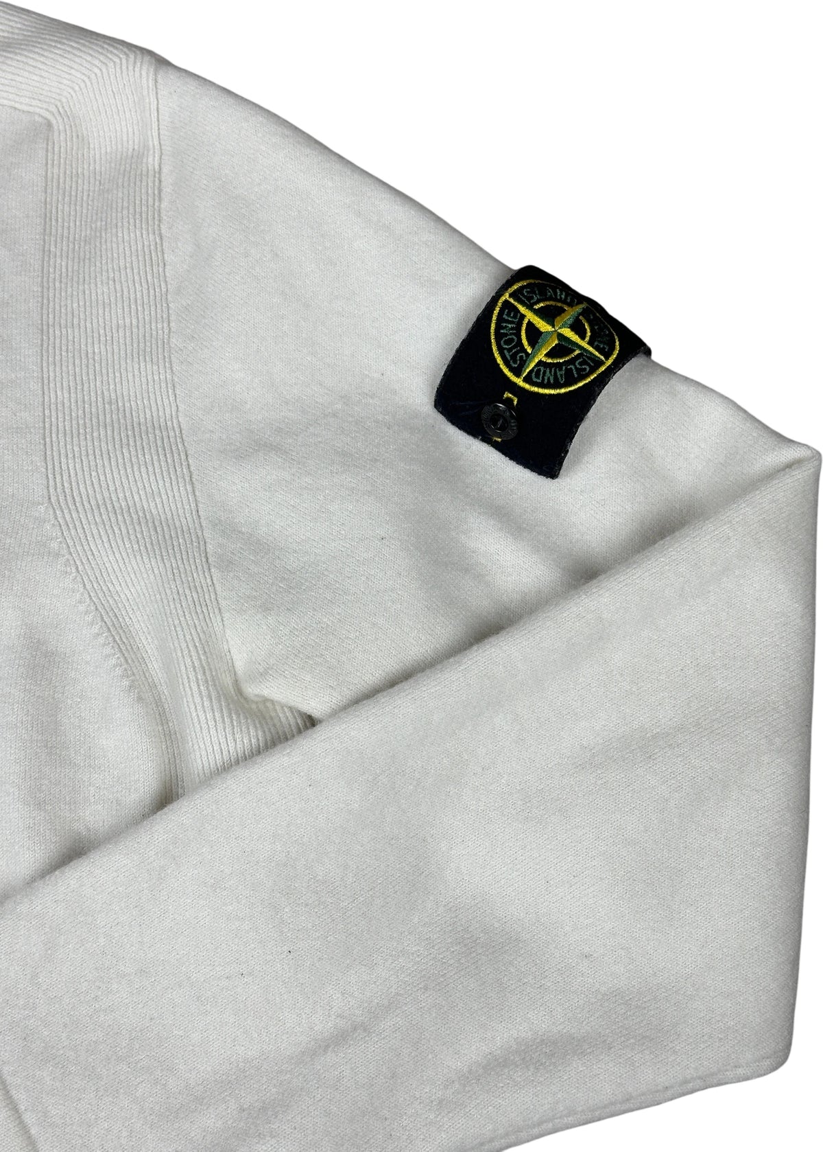 Close-up of a white Stone Island garment sleeve with the brand's signature black compass patch featuring yellow detailing.