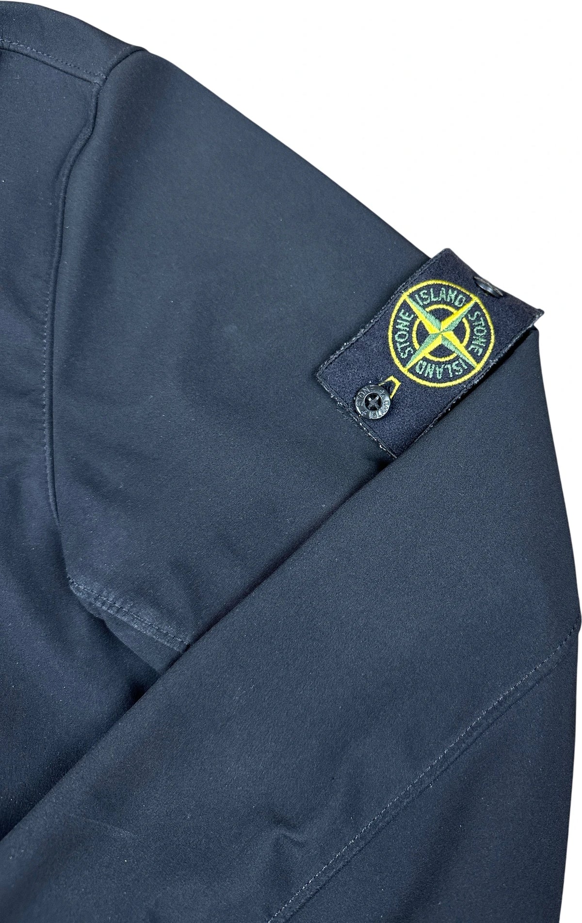 Close-up of a black blue garment sleeve showing the Stone Island logo patch on the shoulder.