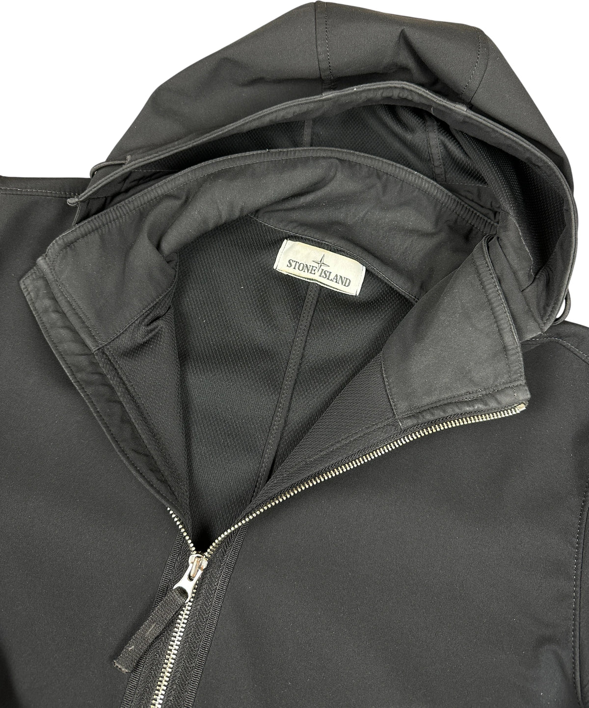 Close-up of a black hooded zip-up jacket with a visible Stone Island neck label, showing the interior lining and zipper details against a plain white background.